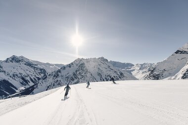 Drei Skifahrer fahren eine breite, frisch präparierte Piste in Gargellen bei Sonnenschein mit Bergpanorama im Hintergrund. | © Gargellner Bergbahnen GmbH & Co KG, Daniel Zangerl