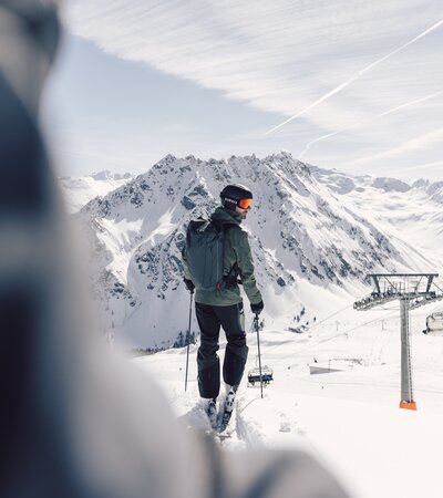 Skifahren in Gargellen | © Gargellner Bergbahnen GmbH & Co KG, Daniel Zangerl Skifahrer mit Helm und Rucksack steht auf einer Piste in Gargellen und blickt ins verschneite Tal, Sessellift im Hintergrund. | © Gargellner Bergbahnen GmbH & Co KG, Daniel Zangerl