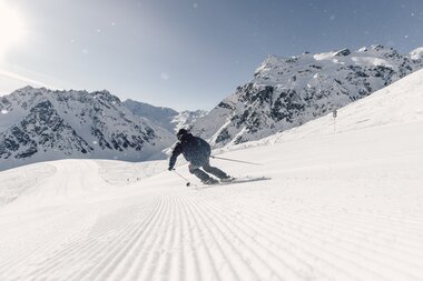 Skifahrer fährt in Schwüngen eine frisch präparierte Piste in Gargellen hinunter, verschneite Bergkulisse im Hintergrund. | © Gargellner Berbahnen GmbH & Co KG, Daniel Zangerl