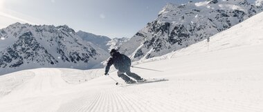 Skifahrer fährt in Schwüngen eine frisch präparierte Piste in Gargellen hinunter, verschneite Bergkulisse im Hintergrund. | © Gargellner Berbahnen GmbH & Co KG, Daniel Zangerl