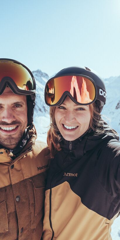 Mann und Frau im Skioutfit machen ein Selfie auf einer sonnigen Skipiste im Skigebiet Gargellen im Montafon, mit verschneiten Madrisa, so heißt der Berg im Hintergrund. | © Gargellner Bergbahnen GmbH & Co KG, Christoph Schöch 