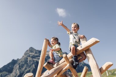 Zwei Kinder klettern auf einem hölzernen Klettergerüst am Spielplatz Schafberg vor der Bergkulisse von Gargellen. | © Gargellner Bergbahnen GmbH & Co KG, Daniel Zangerl