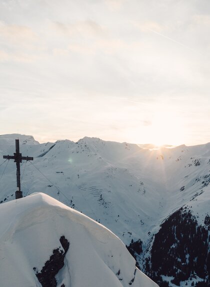 Gipfelkreuz im Morgenlicht mit verschneiten Bergen und Sonnenaufgang über Gargellen. | © Gargellner Bergbahnen GmbH & Co KG, Daniel Zangerl