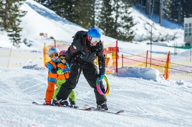 Ein Skilehrer fährt gemeinsam mit zwei kleinen Kindern im Kinderland Ski  | © Schischule Gargellen