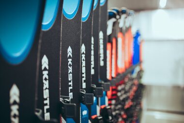 Mehrere Paar Ski der Marke Kästle stehen ordentlich in einer Reihe in einem Skiverleih. Die Vorderseiten der Ski in Blau, Schwarz und Rot sind deutlich zu erkennen. Der Hintergrund des Raums ist unscharf, wodurch der Fokus auf den Ski liegt. | © Gargellner Bergbahnen GmbH & Co KG, Christoph Schöch 