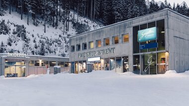 Außenansicht des Gebäudes „PME Shop & Rent“ mit angeschlossenem Skidepot im Skigebiet Gargellen; vor dem modernen Betonbau liegt Schnee, im Hintergrund ein bewaldeter, verschneiter Hang. | © Gargellner Bergbahnen GmbH & Co KG, Daniel Zangerl