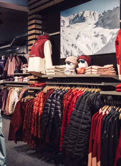 Übersicht über den Innenbereich des PME Shop & Rent mit aufgehängter Wintersportbekleidung in verschiedenen Farben; Jacken, Pullover und Accessoires sind geordnet an Kleiderstangen und Regalen präsentiert. | © Gargellner Bergbahnen GmbH & Co KG, Daniel Zangerl