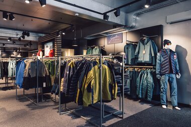 Innenansicht des PME Shop & Rent mit mehreren Kleiderständern für Wintersportbekleidung; Jacken und Hosen sind nach Modellen geordnet ausgestellt, rechts steht eine Schaufensterpuppe mit kompletter Winterausrüstung. | © Gargellner Bergbahnen GmbH & Co KG, Daniel Zangerl