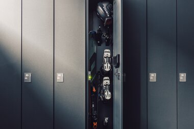 Ein geöffnetes Skidepot zeigt Ski, Skischuhe, Handschuhe und einen Helm ordentlich verstaut in einem schmalen Spind; angrenzende Spinde mit Nummern sind geschlossen. | © Gargellner Bergbahnen GmbH & Co KG, Daniel Zangerl