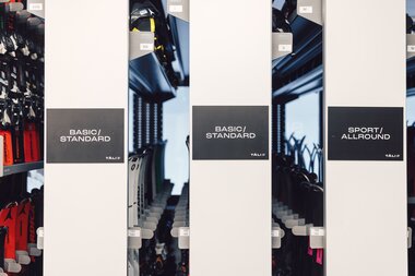 Frontale Ansicht mehrerer Skidepot-Reihen im Sportverleih mit Beschilderungen „Basic / Standard“ und „Sport / Allround“; dahinter sind Skier in verschiedenen Längen und Größen einsortiert. | © Gargellner Bergbahnen GmbH & Co KG, Daniel Zangerl